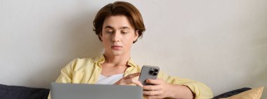 Şık genç adam rahat bir kanepede dinlenirken akıllı telefon ve dizüstü bilgisayar kullanıyor..