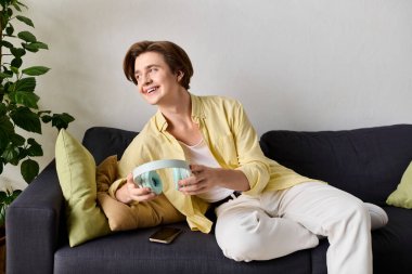 Şık kıyafetli genç adam, kulaklığı sakin ve davetkar bir yerde tutarken gülümsüyor..