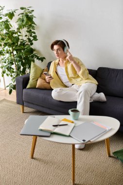 Şık bir genç adam kulaklıklarıyla müzik dinlemekten hoşlanır. Kanepede uzanır, akıllı telefonunu kullanır..