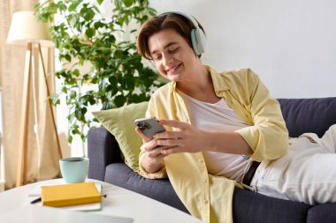 Yakışıklı genç adam kanepede dinleniyor, telefonunda gezinirken müzik dinliyor..