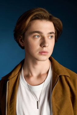 Yakışıklı genç adam düşünceli bir poz veriyor, modaya uygun bir ceket ve sade beyaz bir tişört giyiyor..