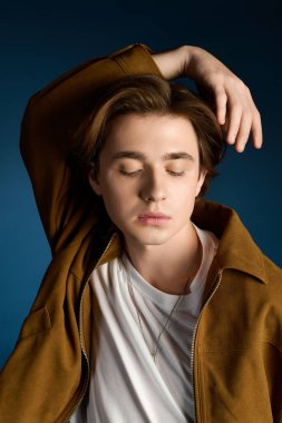 Şık bir genç adam, rahat bir şekilde poz verir. Gözleri kapalı, çekici ve rahat bir şekilde..