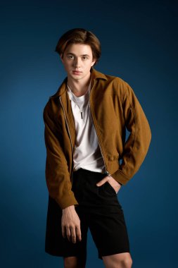 Kendine güveni olan genç bir adam, şortu ve şık bir ceketi olan, modaya uygun bir kıyafet sergiliyor..
