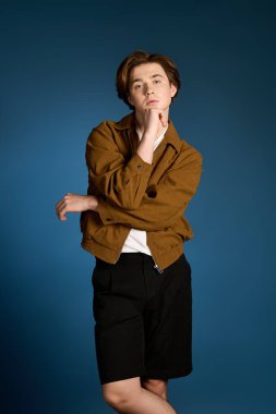 Moda görünümlü genç bir adam kendine güvenerek duruyor, havalı bir stüdyo ortamında modayı yansıtıyor..