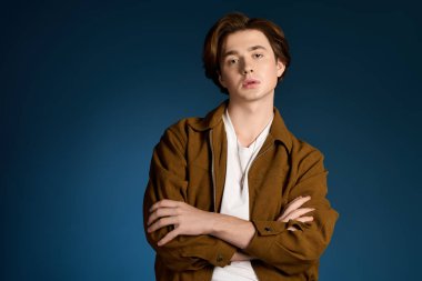 Yakışıklı genç bir adam kollarını kavuşturup şık kıyafetlerini ve rahat tavırlarını sergiliyor..