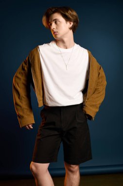 Şık genç adam kendine güvenerek poz veriyor. Mavi arka planda günlük ama modaya uygun kıyafetler giyiyor..