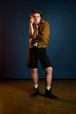 Şık bir genç adam, kendine güvenerek mavi bir zemine karşı poz veriyor, modaya uygun kıyafetinin altını çiziyor.