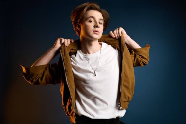 Genç, modaya uygun bir adam, kendine güvenen bir duruşla şık kıyafetini sergileyerek cesurca ayakta duruyor..