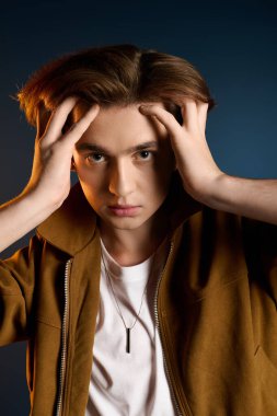 Hareketli bakışları olan modaya uyan genç bir adam ellerini başının üstüne koyar ve tarzını gösterir..