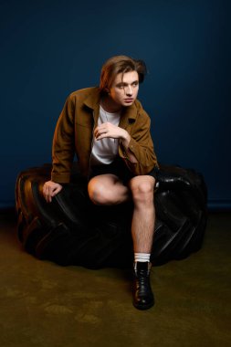 Şık bir genç adam, şık bir stüdyoda büyük bir lastiğin üzerinde kendine güvenle poz veriyor, şehir modasını somutlaştırıyor..