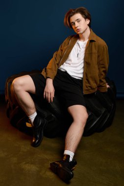 Genç, yakışıklı bir adam büyük bir lastiğe güvenle oturmuş, modaya uygun bir kıyafet ve rahat bir hava sergiliyor..