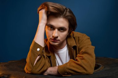 Şık bir genç adam çenesini nazikçe elinin üzerine koyar, canlı renklerin arasında..