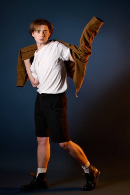 Yakışıklı genç adam stüdyo ortamında şık bir ceket giyerken kendine güvenerek poz veriyor..