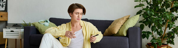 Модный молодой человек удобно сидит в современной гостиной, сосредоточенный на своем смартфоне.