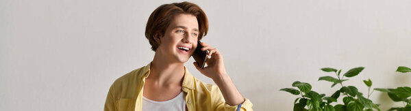 Handsome young man in a casual outfit smiles while talking on the phone near plants.
