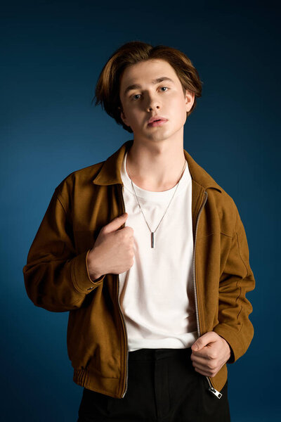 Handsome young man showcases fashionable style with a trendy jacket and relaxed pose indoors.