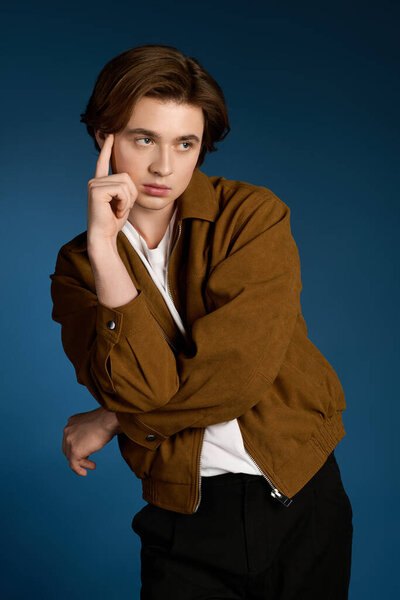 Fashionable young man strikes a thoughtful pose in a trendy outfit with a deep blue background.