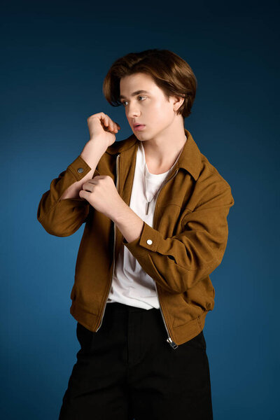 Handsome young man styles a trendy outfit against a striking blue background, preparing for a shoot.