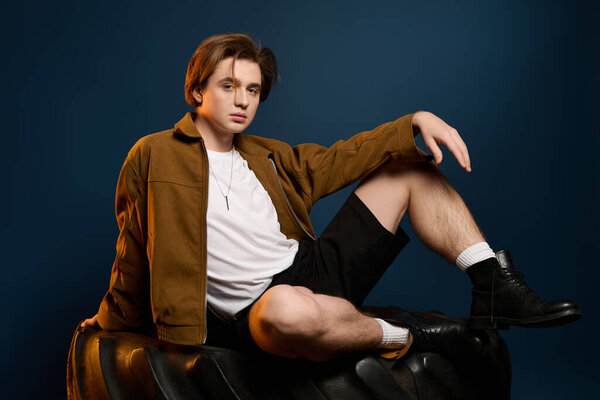 Stylish young man sits on a tire, exuding confidence and fashion in an artistic setting.