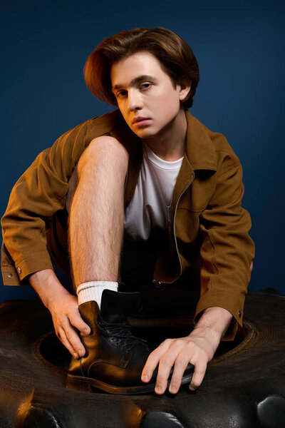 Модный молодой человек преклоняет колени на шине, демонстрируя свой модный вид в студии.