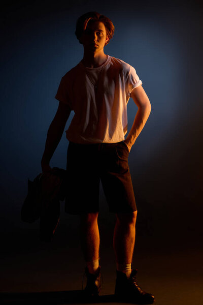 Молодой красивый мужчина уверенно стоит на ярком фоне, источая моду.