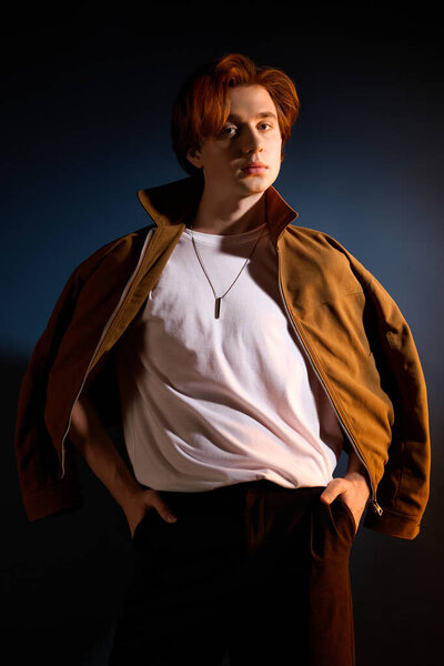 Fashionable young man poses confidently in a trendy outfit against a dark background.