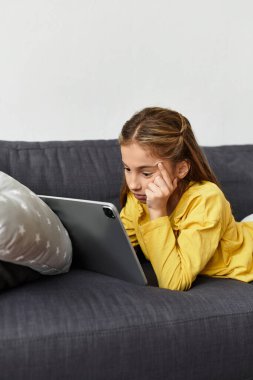 Günlük giysiler içinde bir kız kanepede dinleniyor, tabletinin keyfini çıkarıyor..