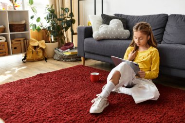 Parlak bir odada tabletini kullanarak rahat bir halının üzerinde rahatlayan alfa bir kızın sıradan bir sahnesi..