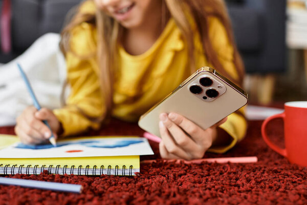 Девушка в повседневной одежде счастливо рисует, пользуясь телефоном дома..