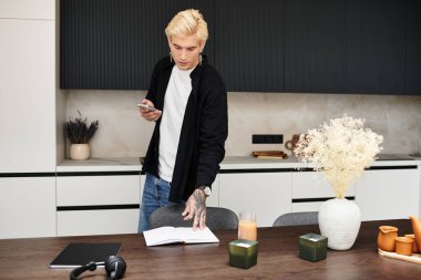 Yakışıklı genç adam şık bir dairede duruyor, bir defter ve telefonla yaratıcılığa dalmış..