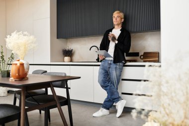 Yakışıklı bir genç adam şık dairesinde mutfak tezgahına yaslanıyor..