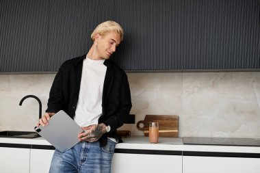 Yakışıklı bir adam şık bir mutfakta mola veriyor, elinde tabletle içkisinin tadını çıkarıyor..