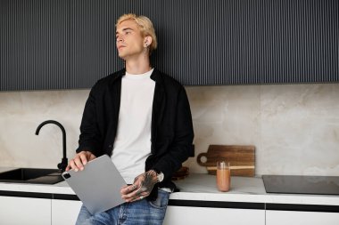 Şık görünümlü genç adam, şık bir mutfak ortamında tablet tutarken rahatlıyor..