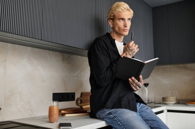 Yakışıklı genç bir adam mutfak tezgahında oturur, bir günlüğe yazarken derin düşüncelere dalmış..