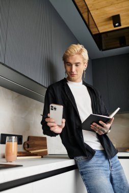 Yakışıklı genç adam şık bir dairede duruyor, telefonuna bakıyor ve not defterine yazıyor..