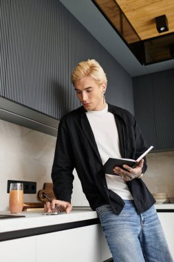 Şık giyinmiş yakışıklı bir adam şık bir mutfakta duruyor, yazarken düşüncelere dalmış..