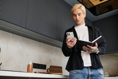 Yakışıklı bir adam şık bir mutfakta duruyor, telefonuna bakıyor ve fikirlerini yazıyor..