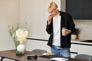 Yakışıklı genç adam modern dairesinde duruyor, sıcak bir pasta ve kahveden zevk alıyor..