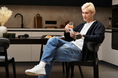 Yakışıklı genç adam şık bir dairede rahatlıyor, meyve suyunu yudumluyor ve telefonunu kontrol ediyor..