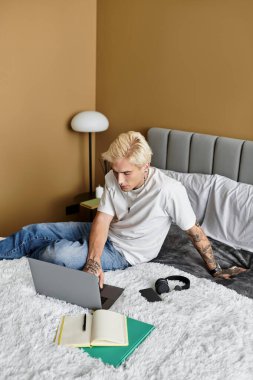 Yakışıklı adam, modern, rahat bir apartman ortamında dinlenirken dizüstü bilgisayarına odaklanıyor..