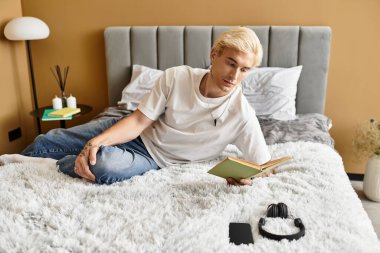 Genç, yakışıklı bir adam kitap okurken yumuşak bir yatakta dinleniyor..