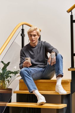 Yakışıklı genç adam merdivenlerde rahatlıyor, rahat bir yerde akıllı telefonuyla meşgul..