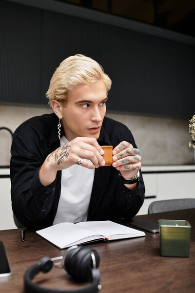 Красивый молодой человек вдумчиво пьет кофе в современной квартире, погруженный в творчество.