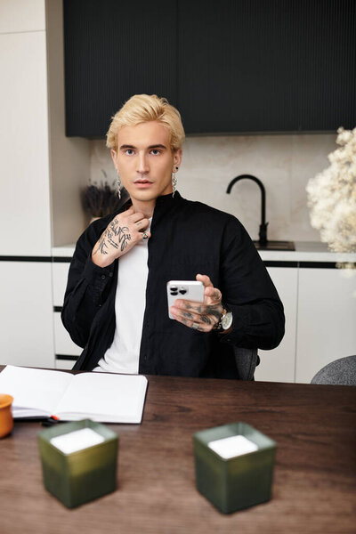 Красивый молодой человек в гладкой квартире проверяет свой смартфон, сидя за деревянным столом.