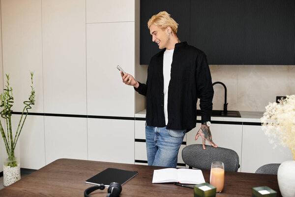 A young handsome man stands in a stylish apartment, smiling as he views his phone screen.