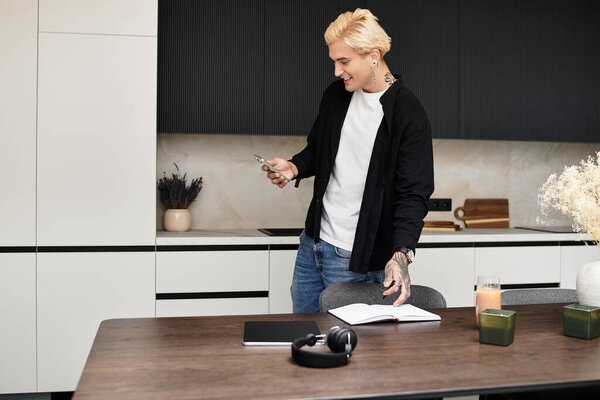 A young, handsome man smiles as he interacts with his phone in a modern apartment.
