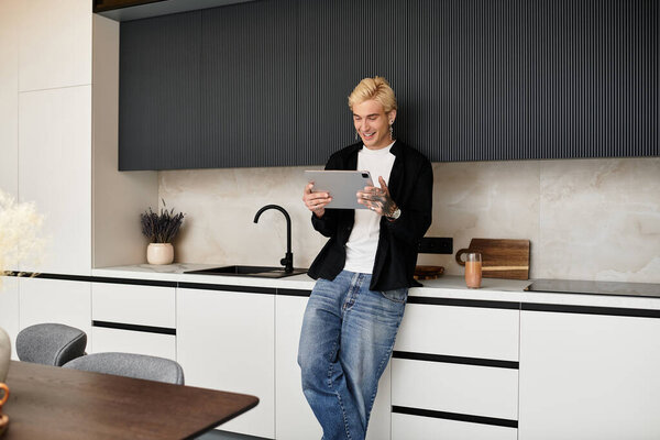 Attractive young man smiles as he engages with his tablet in a stylish urban kitchen.