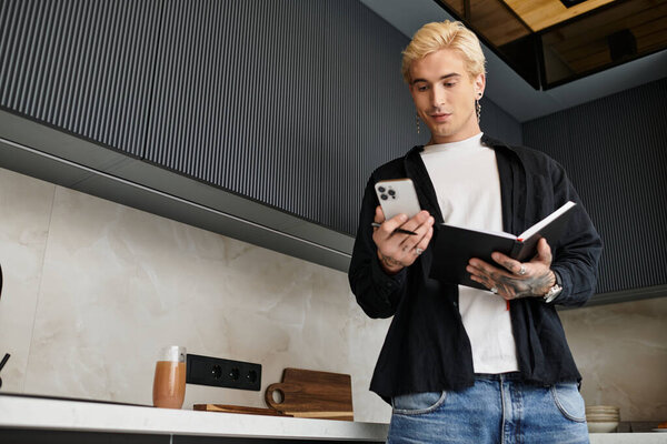 Handsome man stands in a stylish kitchen, glancing at his phone and jotting down ideas.