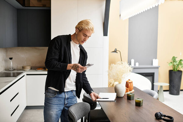 Attractive young man stands in a modern apartment, engaging with his smartphone while relaxing.