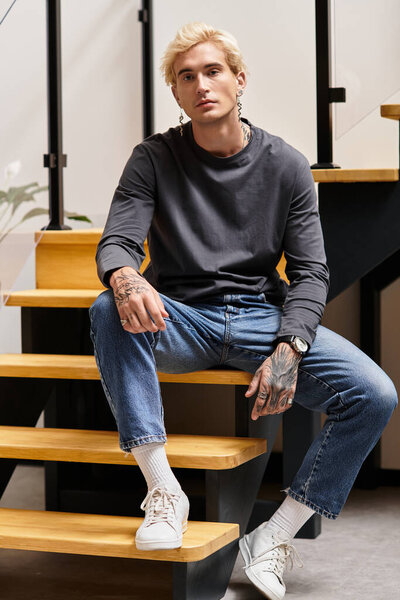 Молодой, красивый мужчина со стильной одеждой расслабился на деревянной лестнице в современном жилом пространстве